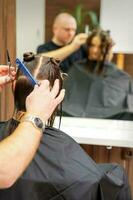 Male stylist cutting the hair of female client in professional beauty salon. photo