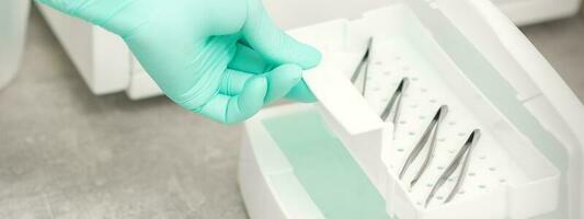 The beautician holds a tray of tweezers preparing them for disinfection with a special liquid and machine. photo