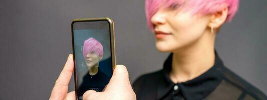 Man hairdresser's hands taking picture on smartphone of her client short pink hairstyle. photo