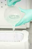 The beautician adds liquid for disinfection of instruments to the machine for sterilization of tools. photo