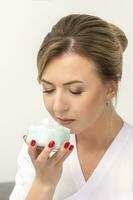 Portrait of young beautician sniffing moisturizing cream holding white jar on white background, copy space. photo