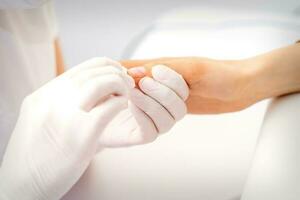 Manicure master wiping the moisturizer from the end of female fingers in beauty salon. photo