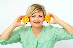 Portrait of young smiling blonde woman cosmetologist with halves of oranges on white background. photo