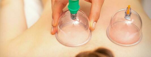 Woman receiving vacuum cupping treatment on back laying on the chest in massage salon. photo