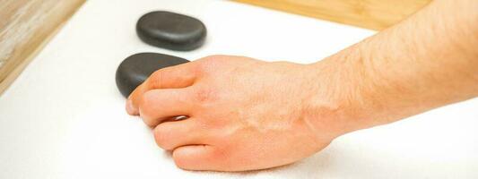 Hand of masseur takes black massage stones from the table in spa salon. photo