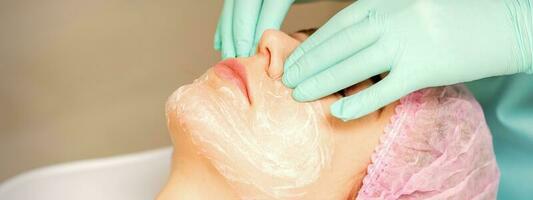 A cosmetologist is applying cream on the female face, close-up view. Woman with doctor beautician in beauty clinic. photo