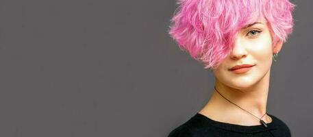 Portrait of beautiful young white woman with a pink short hairstyle on dark background with copy space. photo