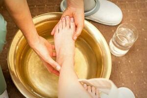 Washing female foot in a special container by male masseur in spa salon. photo