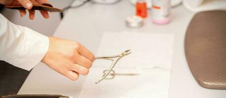 Nail nippers in the hand of female manicure master putting to the towel before nail care in manicure salon. photo