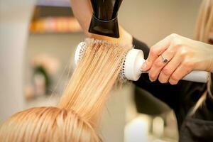 profesional peluquero seco pelo con un secador de pelo y redondo cepillo para el pelo en un belleza salón. foto