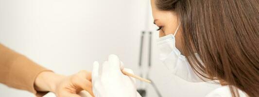 Manicure master in protective face mask and white gloves apply polish to female fingernails. photo