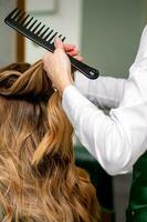 A female hairdresser is combing the long brown hair of a young woman at a parlor. photo