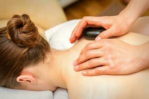 Hot stone massage therapy. Caucasian young woman getting a hot stone massage on back at spa salon. photo