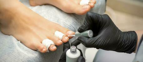 pedicuro aplicando transparente barniz a el hembra uñas de los pies en un belleza salón. foto
