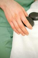 Close up of masseur's hand wipes black massage stones with a white towel. photo