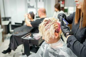 The professional hairdresser uses a brush to apply the pink dye to the hair. Hair coloring concept. photo