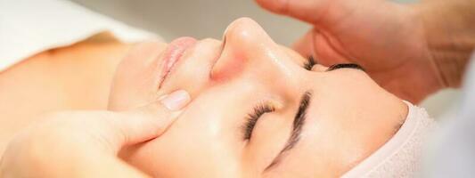 Beautician making lymphatic drainage face massage or facelifting massage at the beauty salon. photo