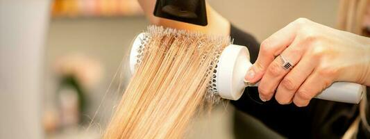 Professional hairdresser dry hair with a hairdryer and round hairbrush in a beauty salon. photo