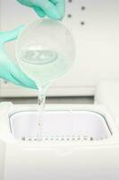 The beautician adds liquid for disinfection of instruments to the machine for sterilization of tools. photo