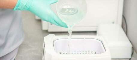 The beautician adds liquid for disinfection of instruments to the machine for sterilization of tools. photo