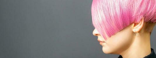 Profile portrait of a young caucasian woman with pink bob haircut isolated on a gray background, copy space. photo