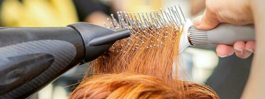 de cerca de maestría mano con secado con aire y cepillo para el pelo soplo hembra rojo pelo en un salón. foto