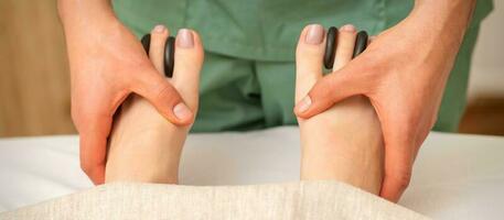 Massager doing feet and toes massage with rocks between a female toes. photo