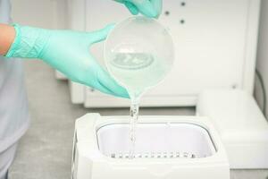 The beautician adds liquid for disinfection of instruments to the machine for sterilization of tools. photo