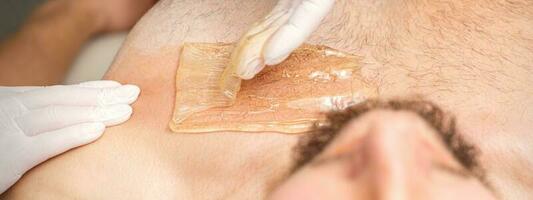 Young caucasian man receiving hair removal from his chest in a beauty salon, depilation men's torso. photo