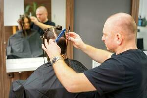 masculino estilista corte el pelo de hembra cliente en profesional belleza salón. foto