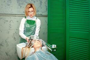 Barber young woman washes a client's head in the sink during the dyeing hair. photo