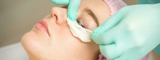 Young woman receiving eyelash removal procedure and removes mascara with a cotton swab and stick in a beauty salon. photo