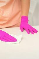 Close up of hands in rubber protective pink gloves cleaning the white surface with a white rag. photo