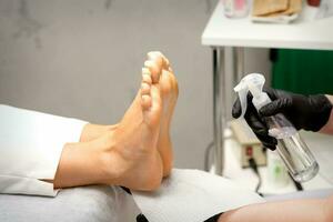 Pedicure master disinfects the feet of woman with the preparation decontamination in beauty salon. photo