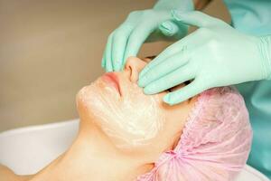 un cosmetóloga es aplicando crema en el hembra rostro, de cerca vista. mujer con médico cosmetólogo en belleza clínica. foto