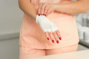 Cosmetologist in workwear wearing white bamboo fingerless gloves on her hands. photo