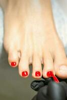 Pedicurist applying red nail polish to the female toenails in a beauty salon. photo