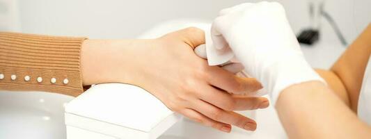 manos de un manicuro en blanco protector guantes limpiar hembra uñas con un papel servilleta en el salón. foto