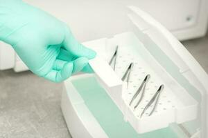 The beautician holds a tray of tweezers preparing them for disinfection with a special liquid and machine. photo