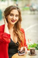 Portrait of a young white woman sitting at the table with a smartphone and looking at camera outdoors. photo