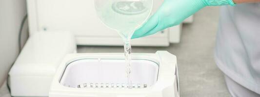 The beautician adds liquid for disinfection of instruments to the machine for sterilization of tools. photo