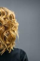 Back view of the woman with long brown curly hair stands on a dark background. photo