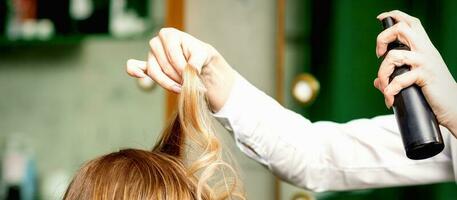 Female coiffeur fixing hairstyling of blonde woman with hairspray in a beauty salon. photo
