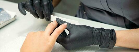 Woman receiving a manicure with nail file by a manicure master in a nail salon. photo