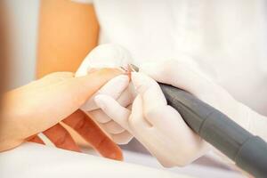 Closeup of manicure master in white gloves applying an electric nail file drill to remove the nail polish in the beauty salon. photo