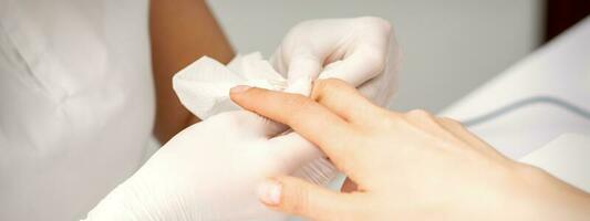 Manicure master wiping the moisturizer from the end of female fingers in beauty salon. photo