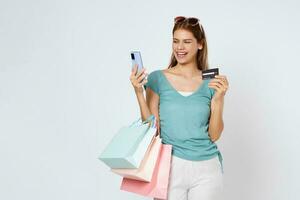 Happy young woman carrying shopping bags with using credit card and mobile phone standing over isolated on white background. photo