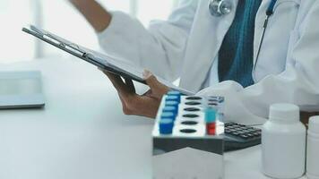 Medical worker in lab coat and sterile mask, doing a microscope analysis while her colleague are working behind video