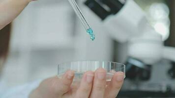 Medical worker in lab coat and sterile mask, doing a microscope analysis while her colleague are working behind video