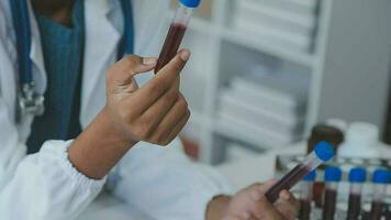 médico trabajador en laboratorio Saco y estéril mascarilla, haciendo un microscopio análisis mientras su colega son trabajando detrás video